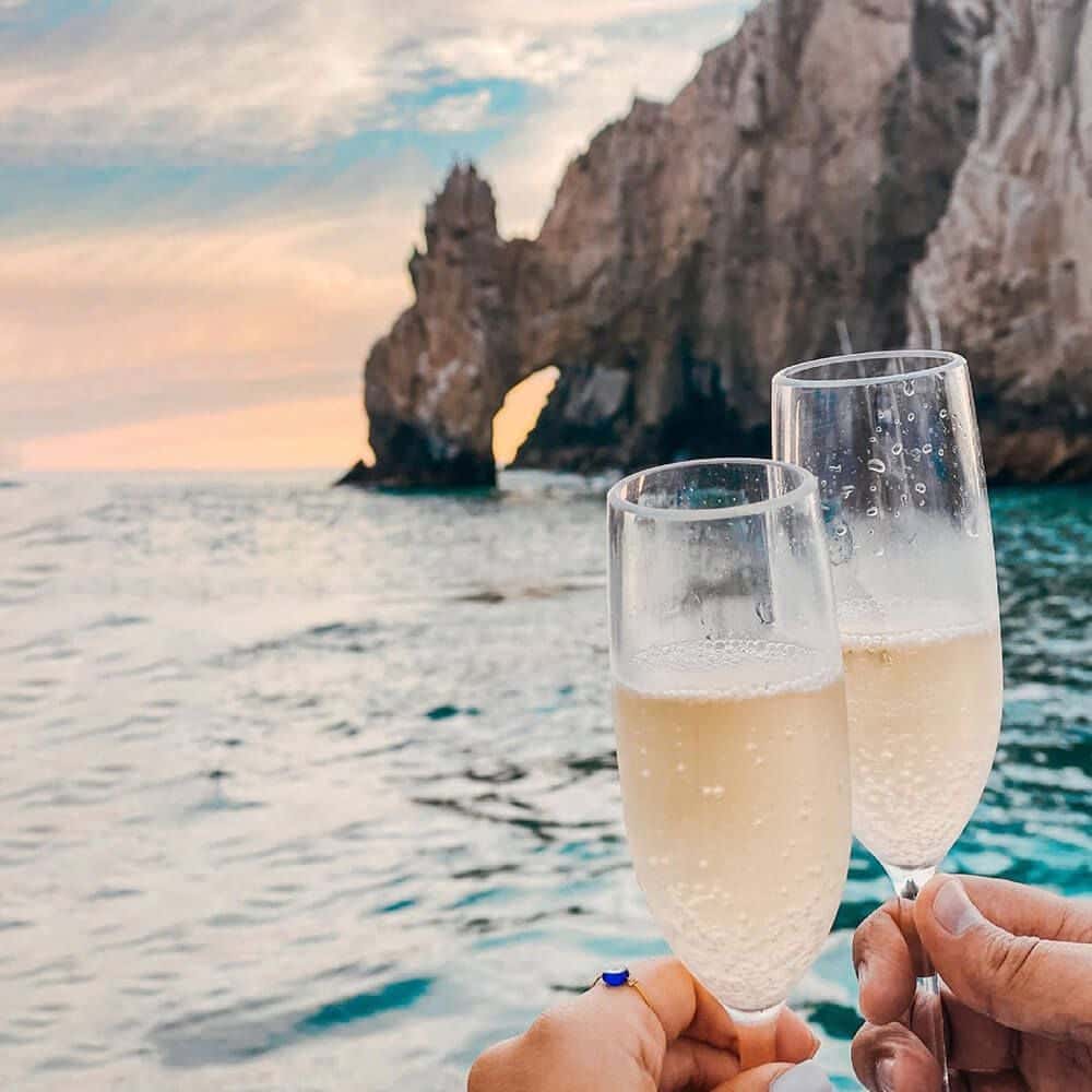 Two champagne glasses raised in a toast, the Arch rock behind