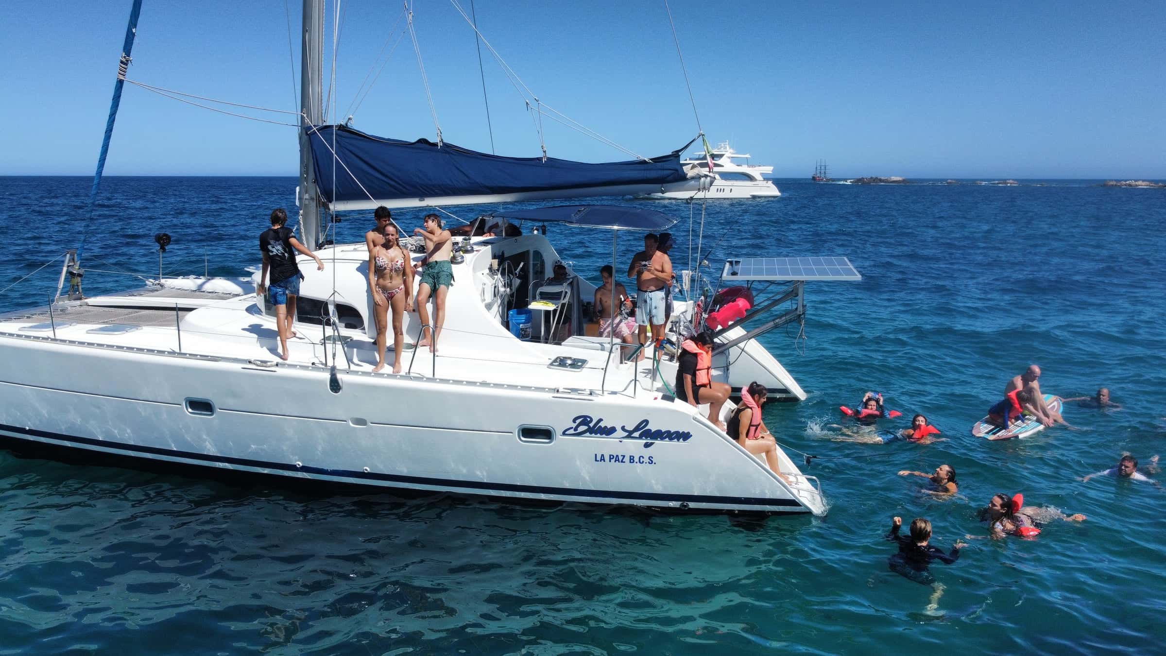 Guests on deck and snorkellers in clear water beside the hull