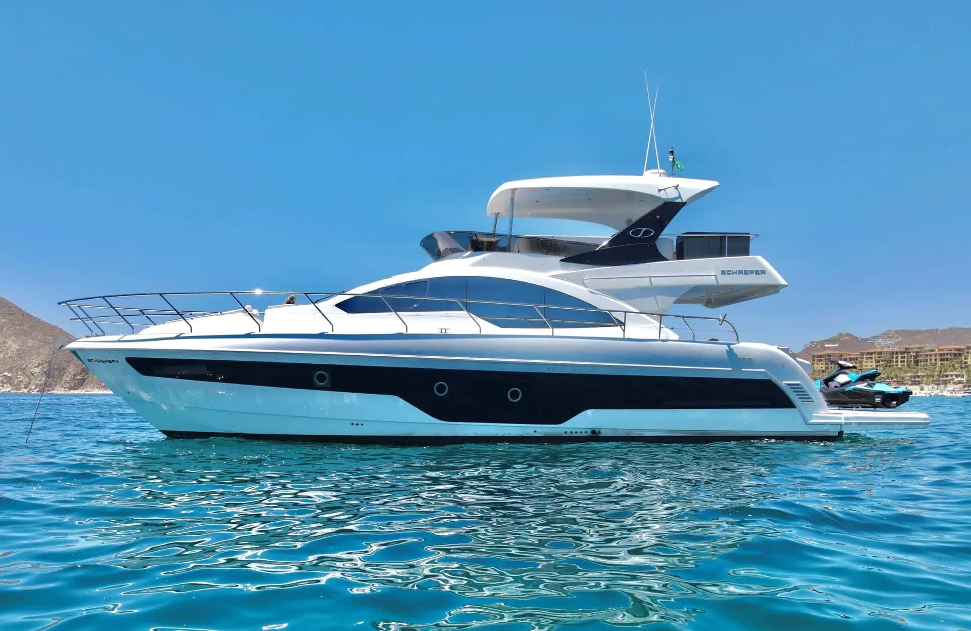 The yacht in profile on turquoise water with a jet ski astern