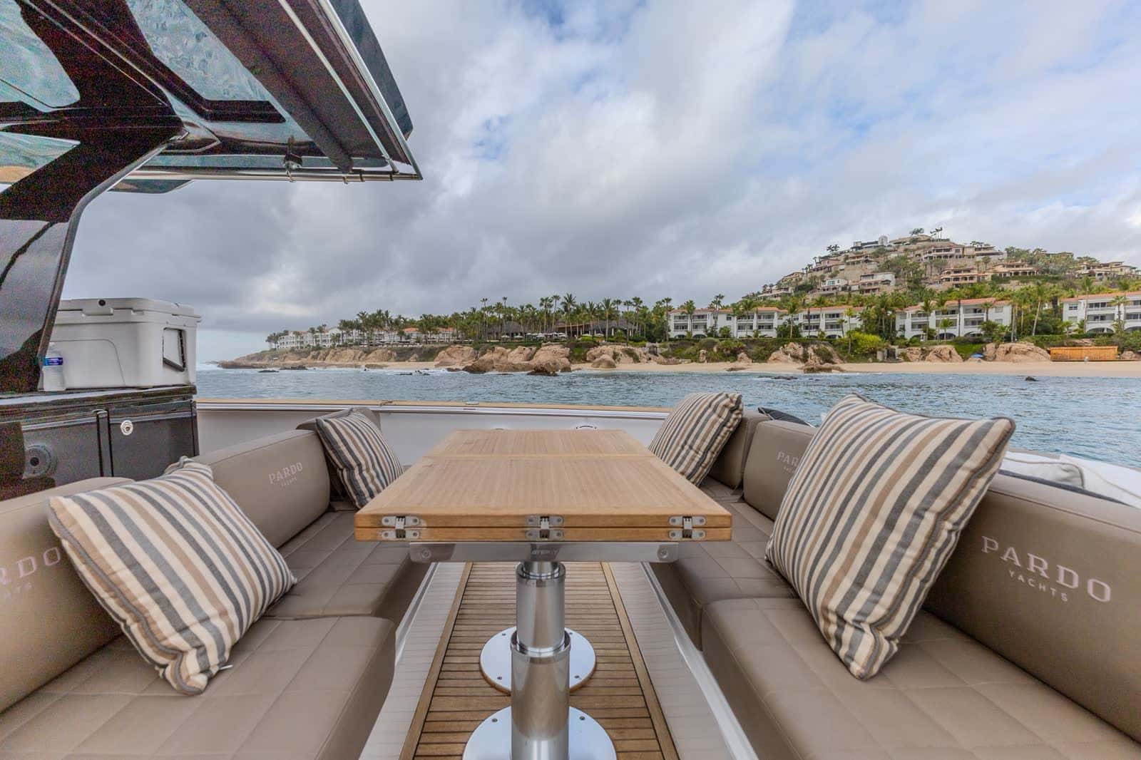 Cockpit sofas with striped cushions around a teak table under the T-top, a hillside of villas across the water