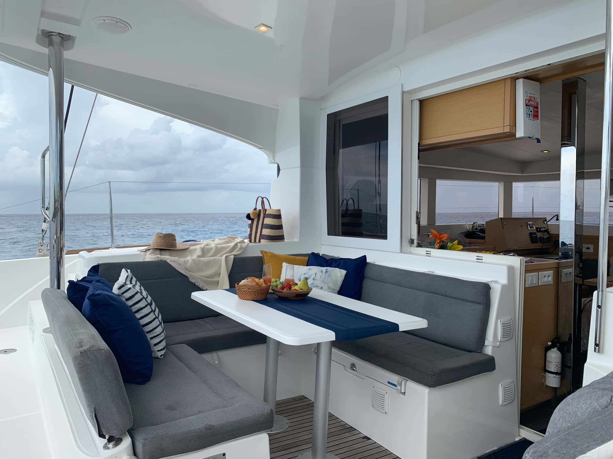 Cockpit table with grey and navy cushioned benches, the galley through the open saloon door