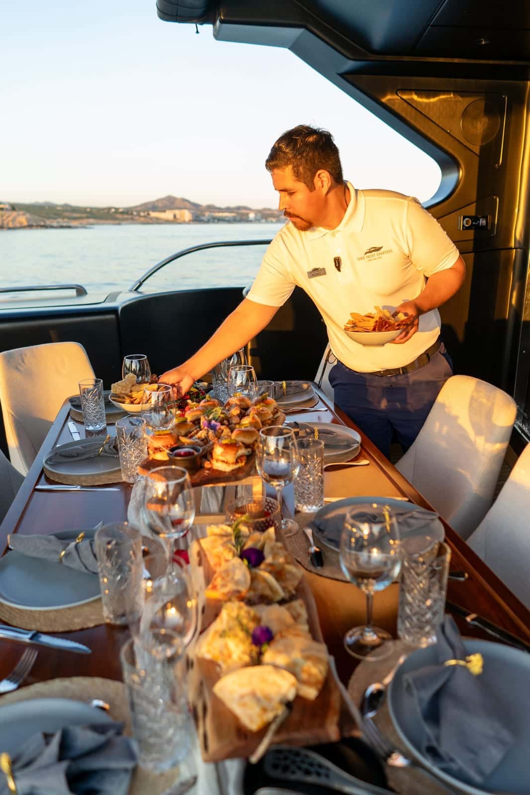 A crew member setting a table on the aft deck at sunset, with sliders and quesadillas on boards