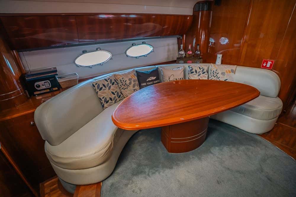 Saloon dinette with a curved cream sofa round an oval wood table and portholes above