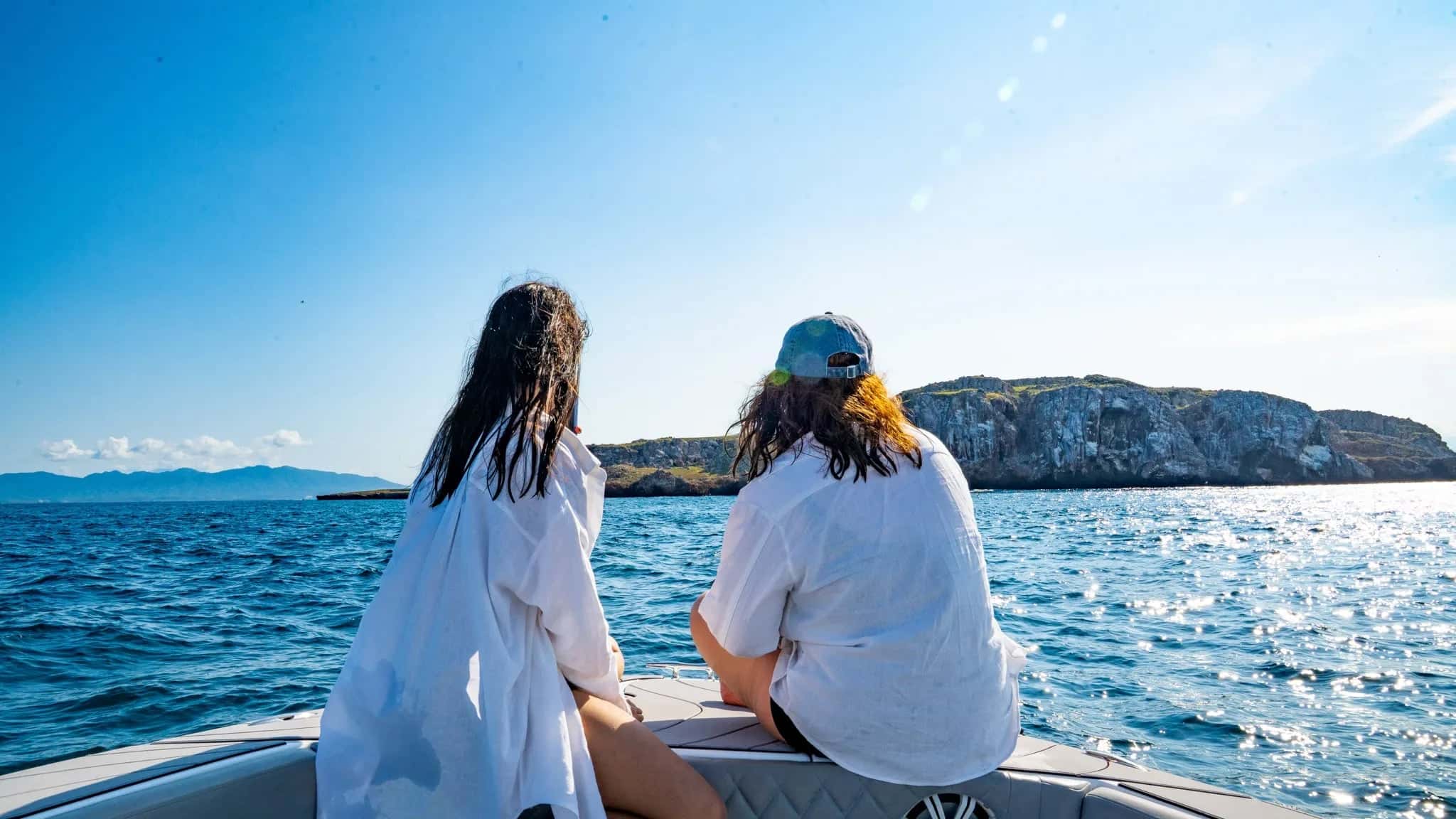 Two guests in white sitting on the bow, looking out at rocky islands