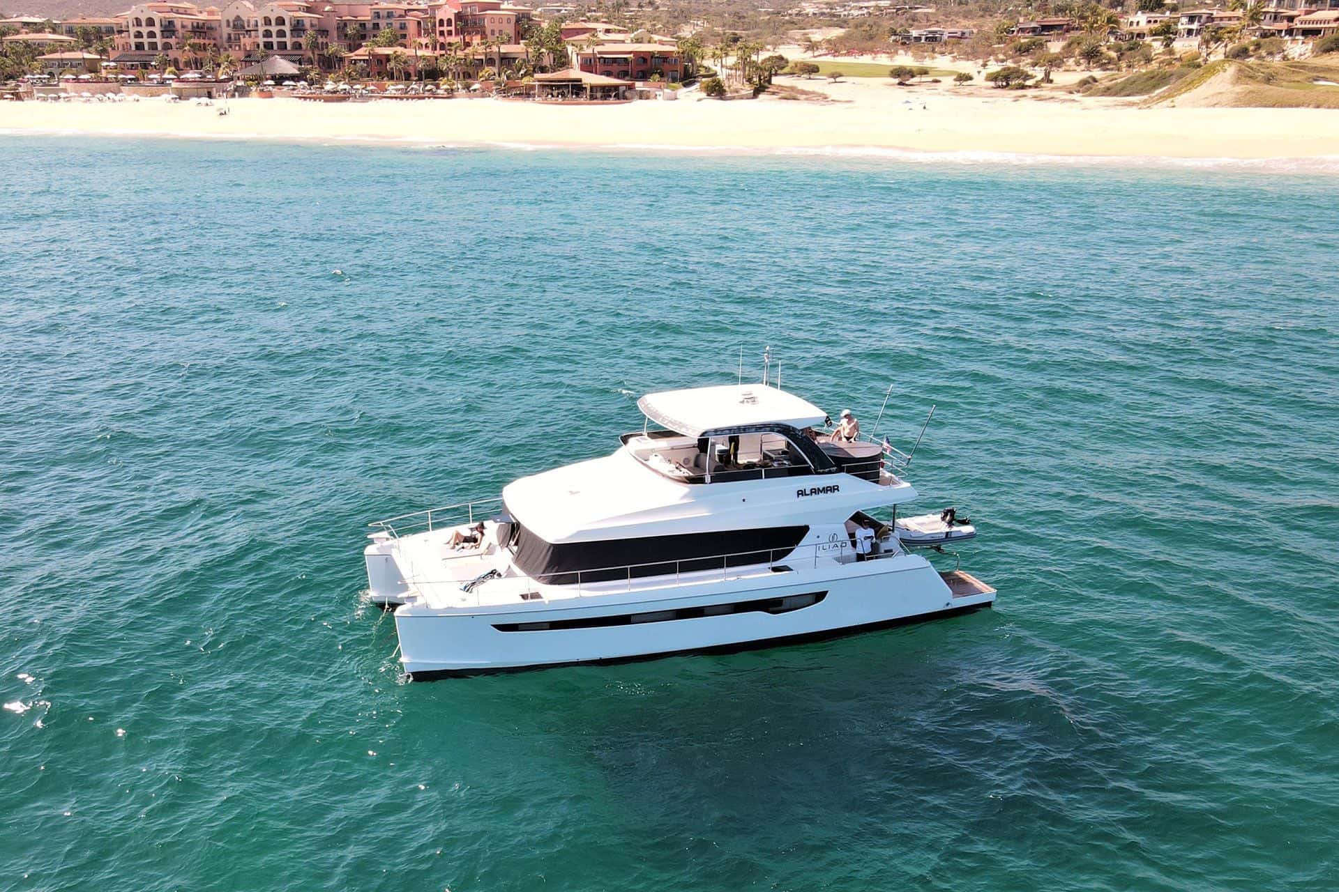 Catamaran from above in green shallows off a sandy beach and low hills
