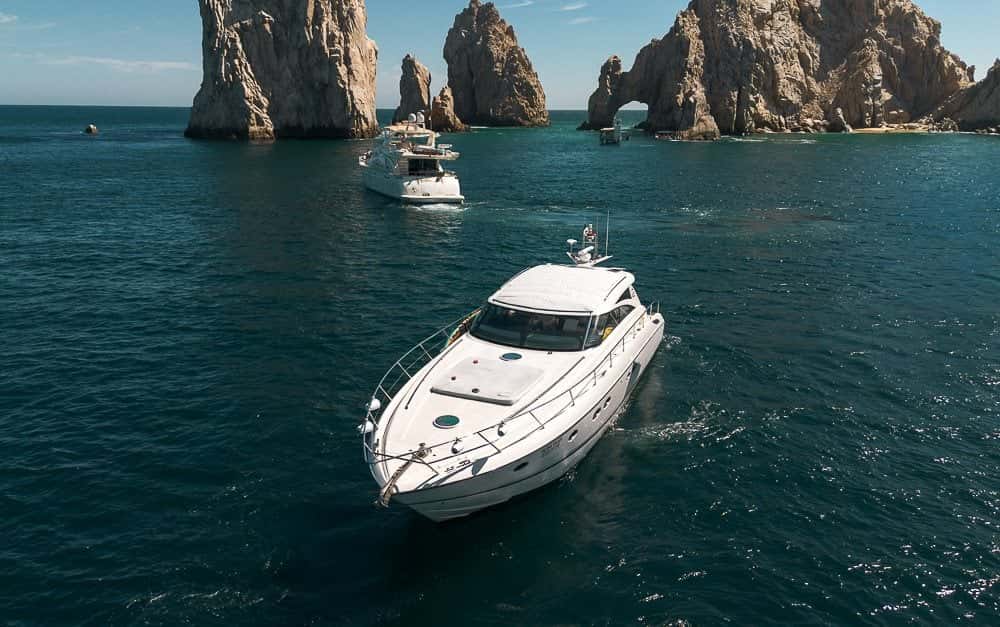 Aerial view of the white sport yacht on dark water below the rock arch and its pinnacles