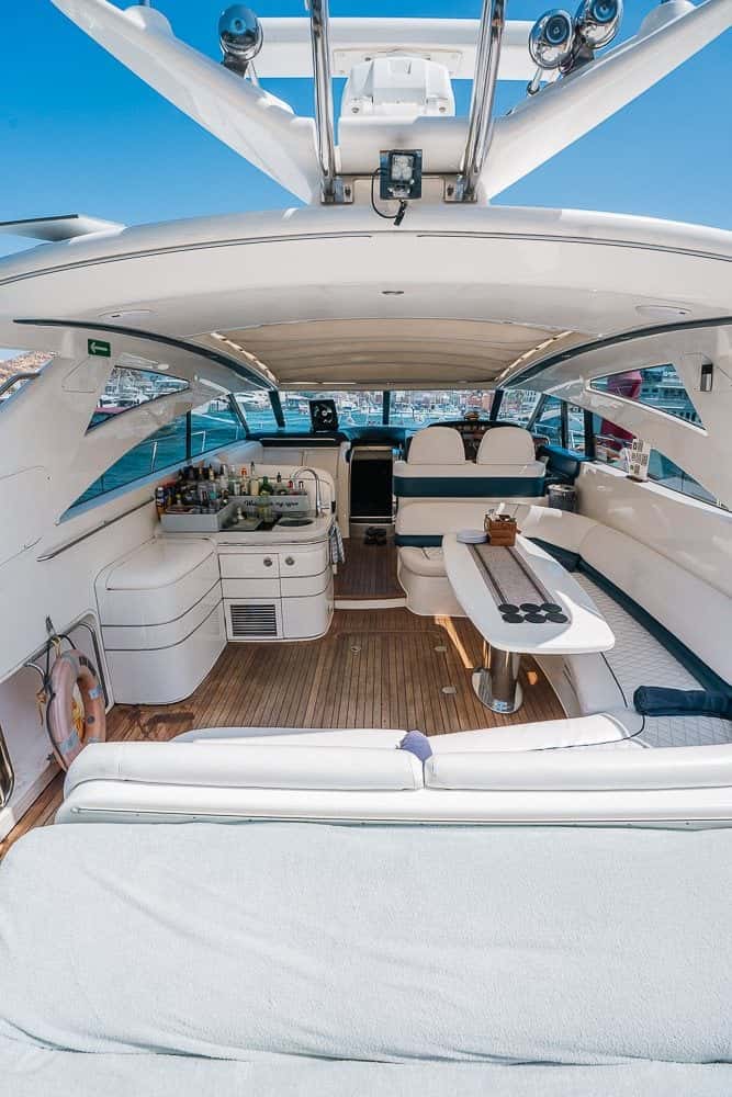 Looking forward through the cockpit: a sun pad, white seating and a dining table under the glass-roofed hardtop