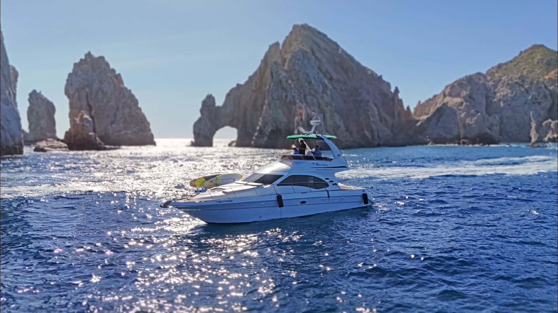 The white flybridge yacht under way on sparkling blue water, the Arch and the rocks of Land's End behind her