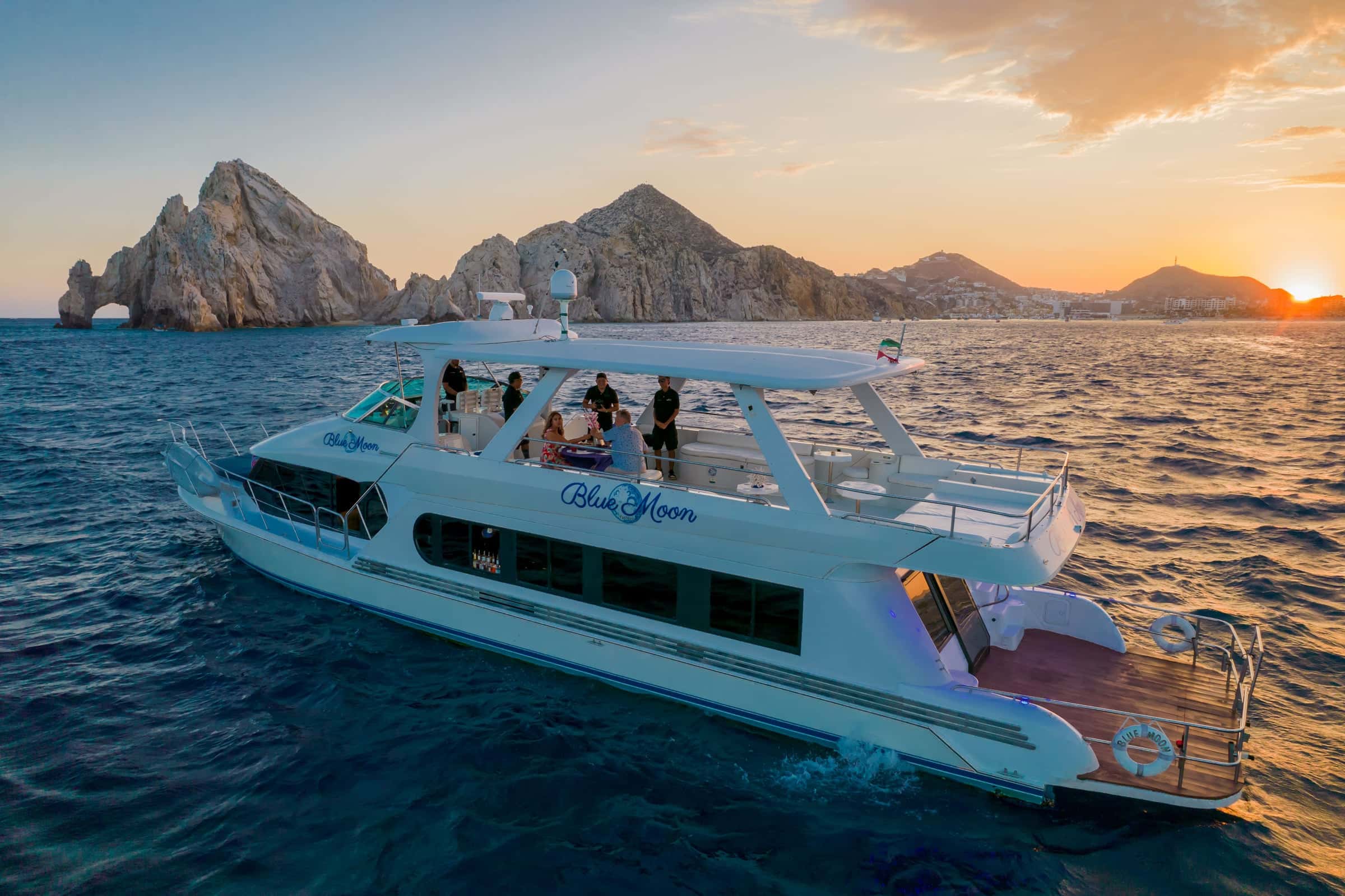 Guests on the upper deck as the yacht cruises past the arch at sunset