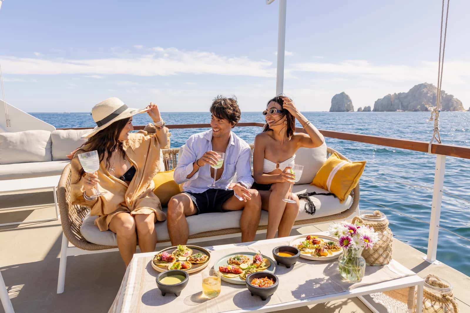 Three guests on a deck sofa over plates of tacos and salsas, the Arch rocks behind