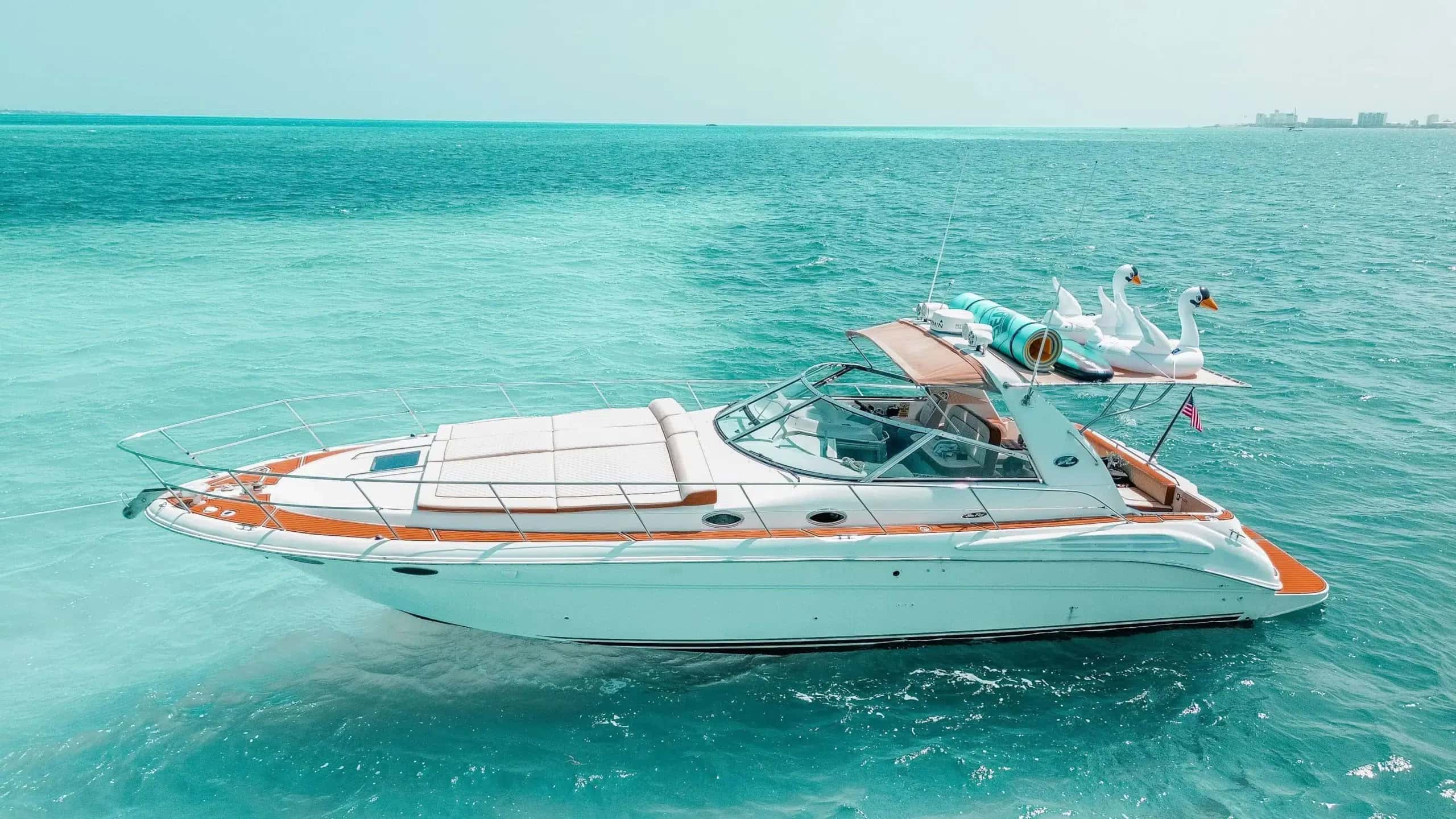 Seañorita at anchor in full side profile, swan floats on the hardtop rack, turquoise water and the hotel zone behind