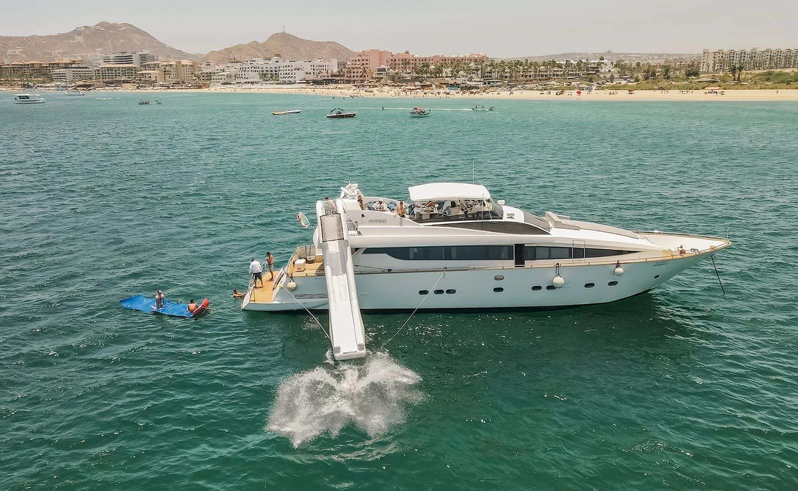 Inflatable slide off the stern into green water, a floating mat beside it and a beach behind