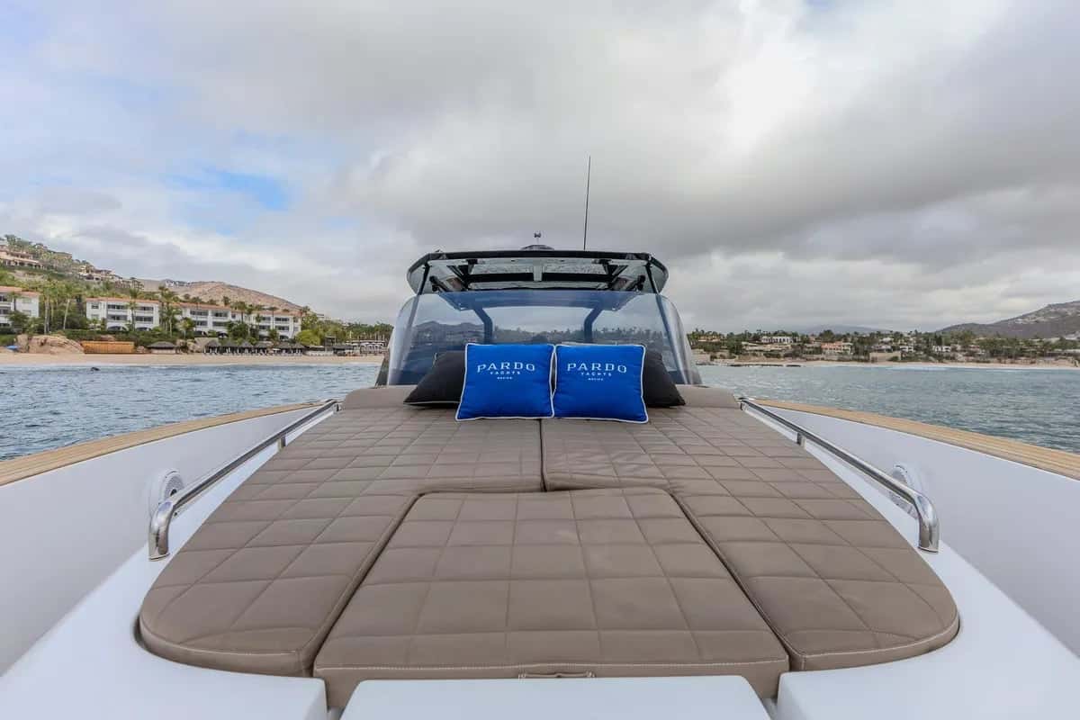 Bow sunbed with two blue Pardo pillows, the windscreen and T-top behind and a resort shore beyond