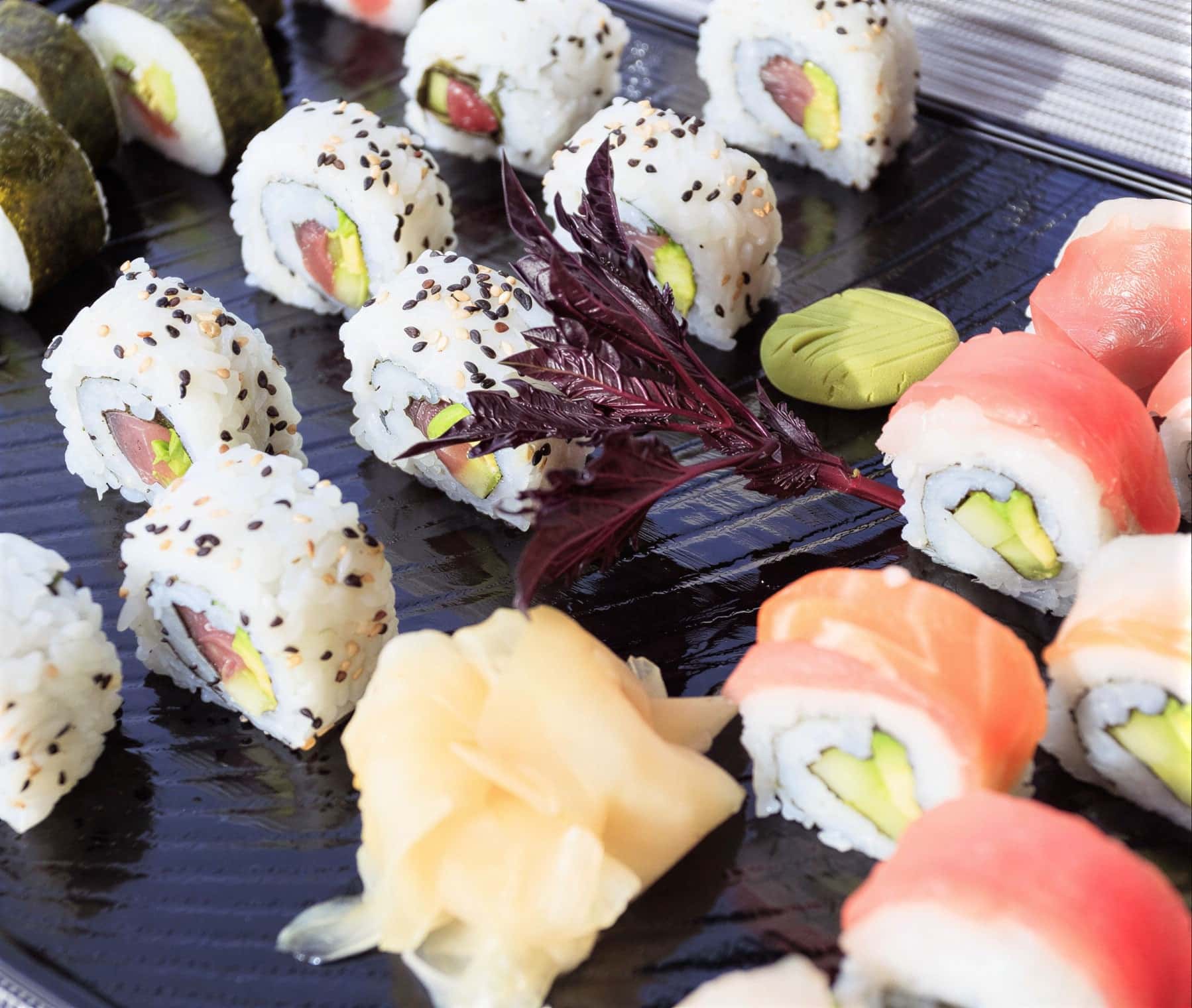 Sushi rolls of salmon, tuna and avocado with pickled ginger and wasabi on a dark platter
