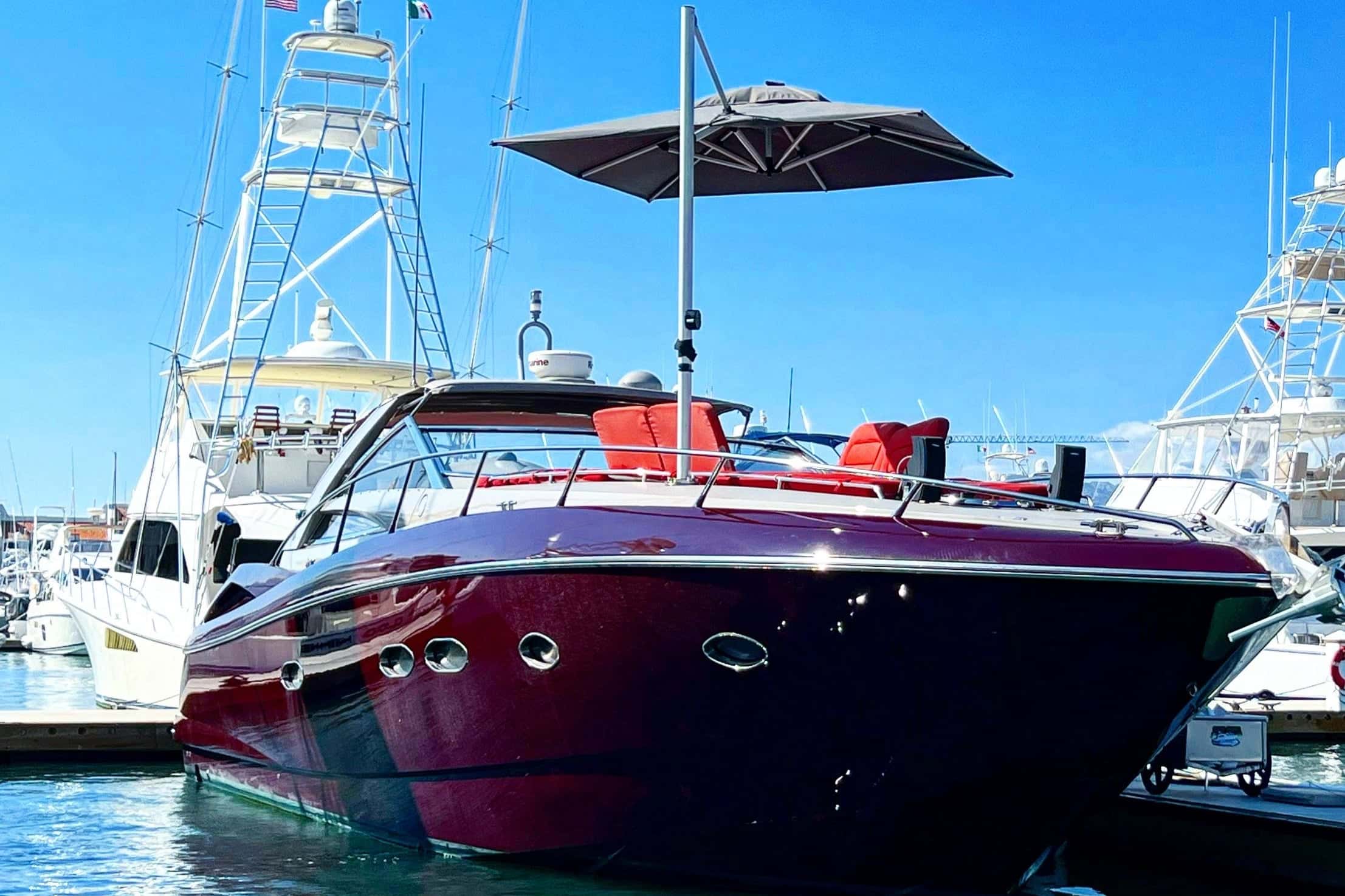 Dark red hull and bow seen from the water in a marina, a shade umbrella raised over the deck and sportfishers alongside