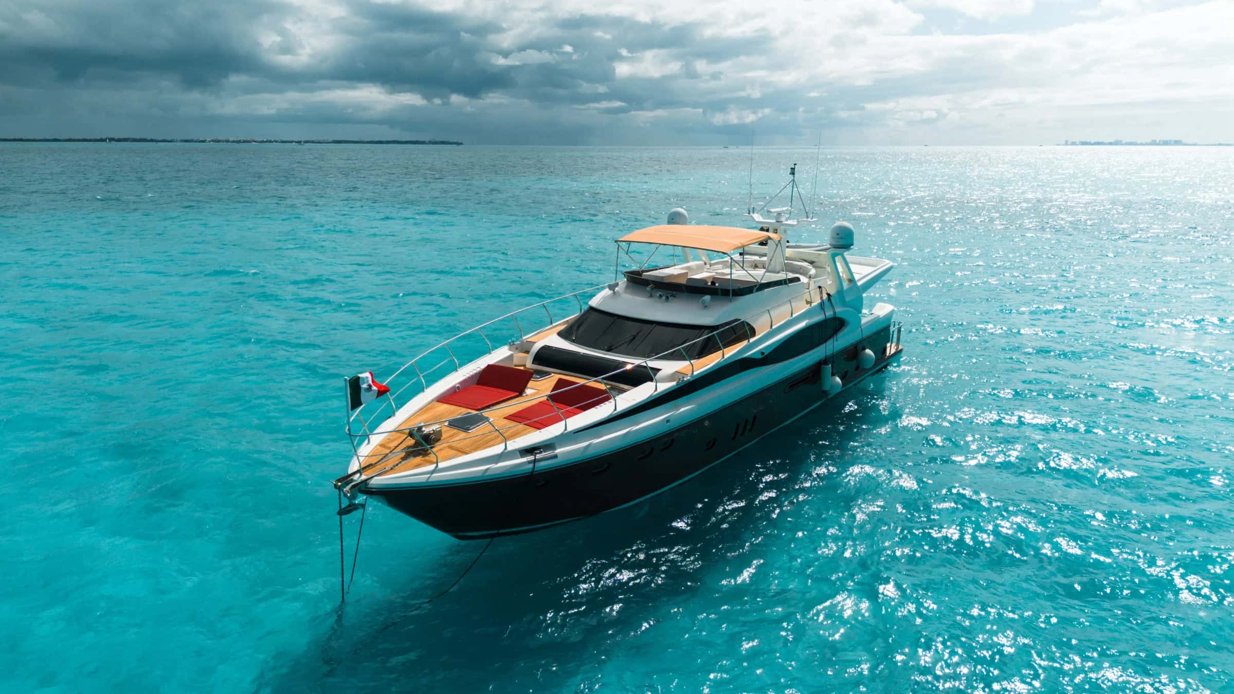 Vive at anchor seen low from ahead, red sunpads on the teak foredeck and the flybridge bimini above