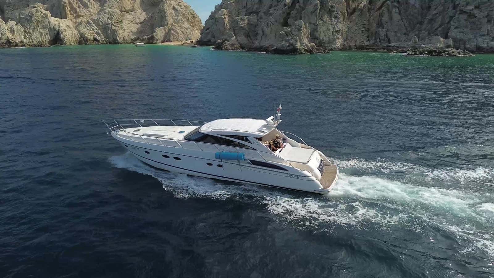 Olivia Grace under way past the granite cliffs at Land's End, a wake curling behind