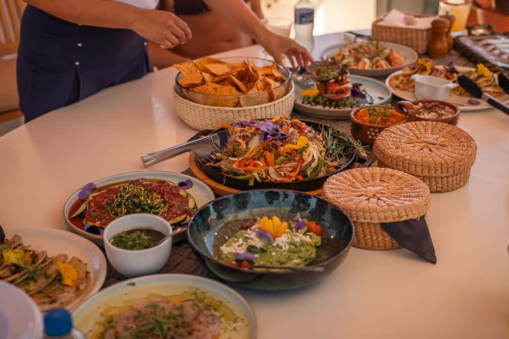 A table of tostadas, guacamole, fajitas in a skillet, a tuna tiradito and chips in woven baskets