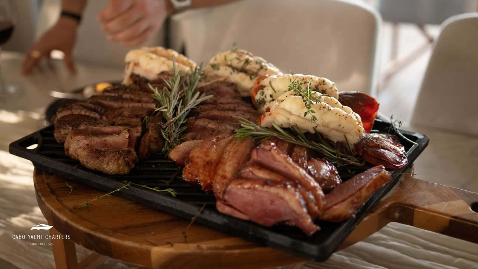 Sliced steak, glazed duck and lobster tails with rosemary on a cast-iron grill plate