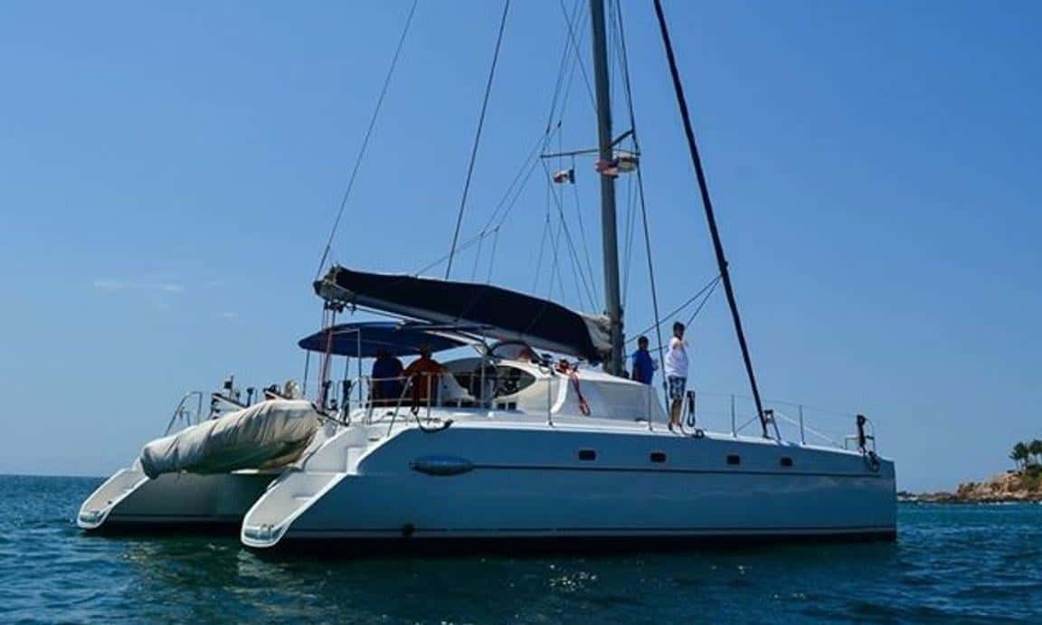 The catamaran under way on calm blue water, bimini up and guests on deck
