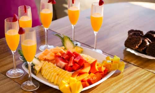 Breakfast on the table: a platter of cut papaya, watermelon and pineapple, glasses of orange juice and a plate of coffee cake