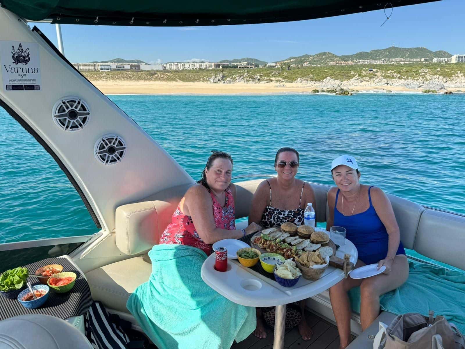 Three guests at the flybridge table over a platter of tacos, under the canopy with a beach and hills behind