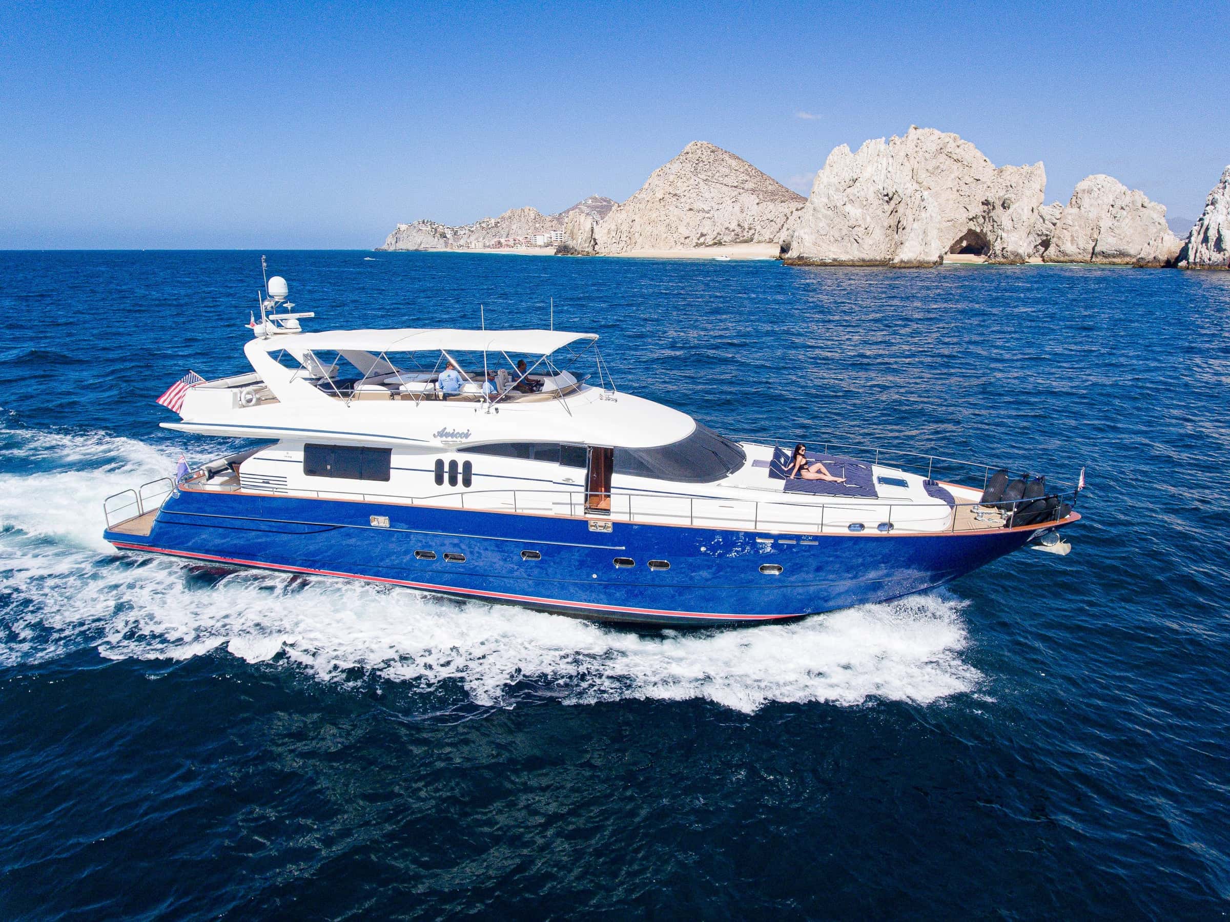 Avicci at speed on deep blue water, a white wake behind and the Land's End rocks on the horizon