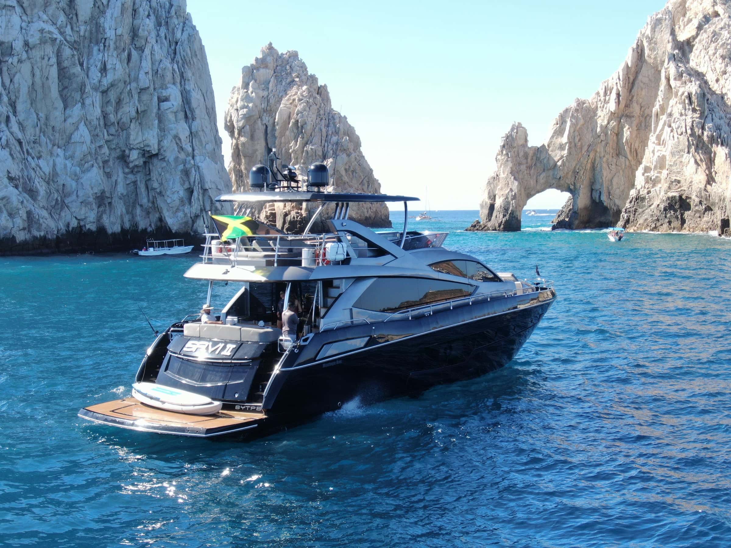 The yacht from astern in front of the rock arch, her swim platform lowered toward the water