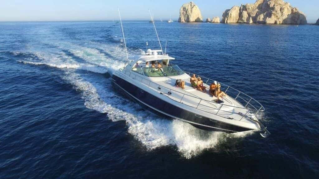 Happy Ending under way at speed on deep blue water, guests on the bow and the cape's rock pinnacles behind