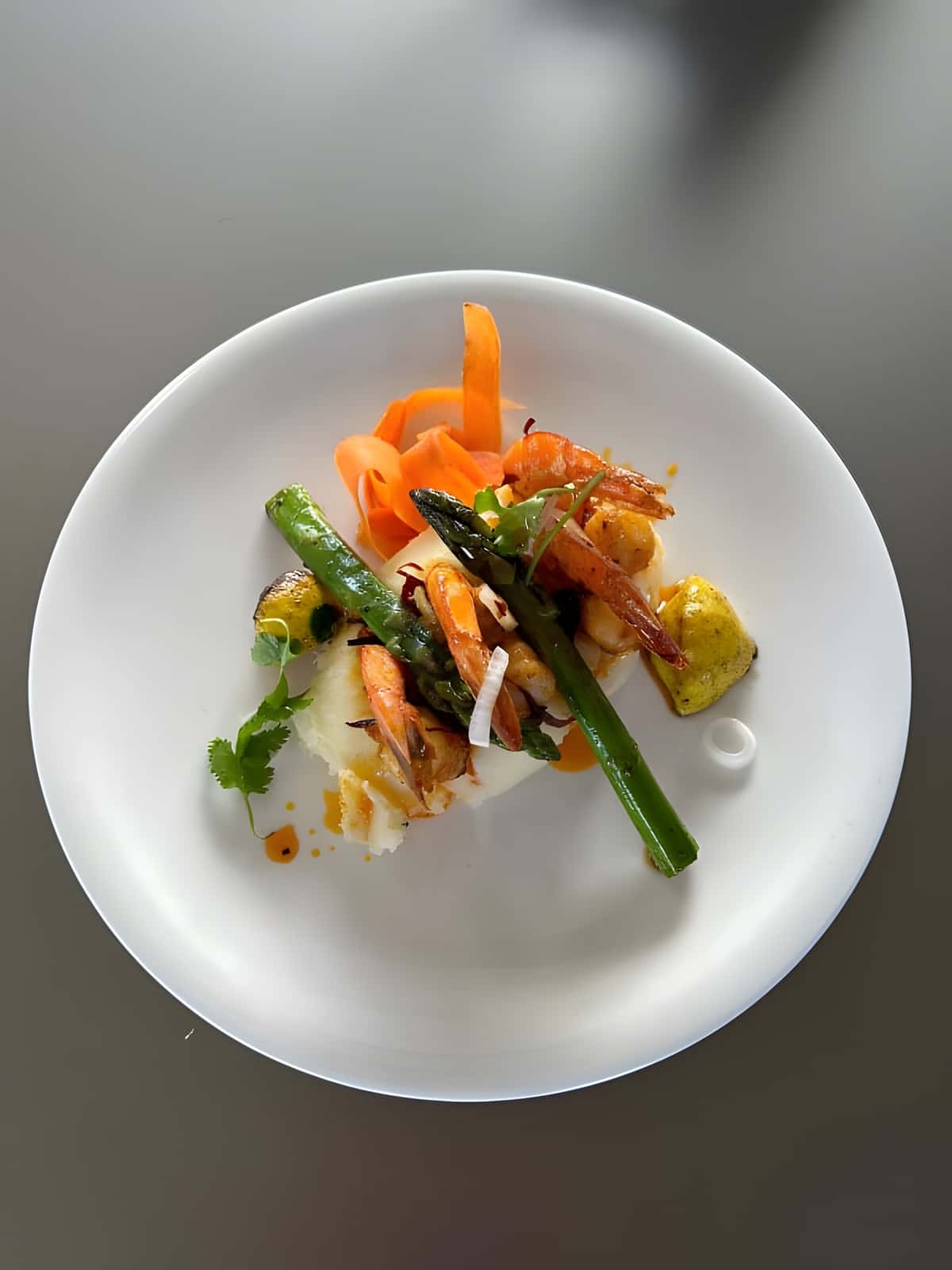 Plated shrimp with grilled asparagus and carrot ribbons on a white plate