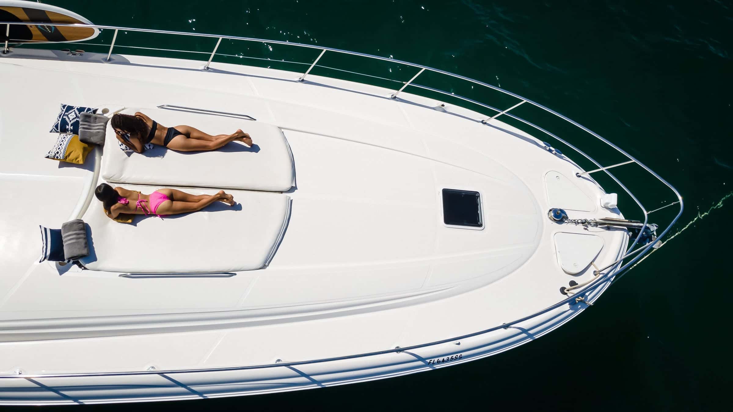 Straight down on the foredeck: two guests sunbathing on towels on the bow sun pads