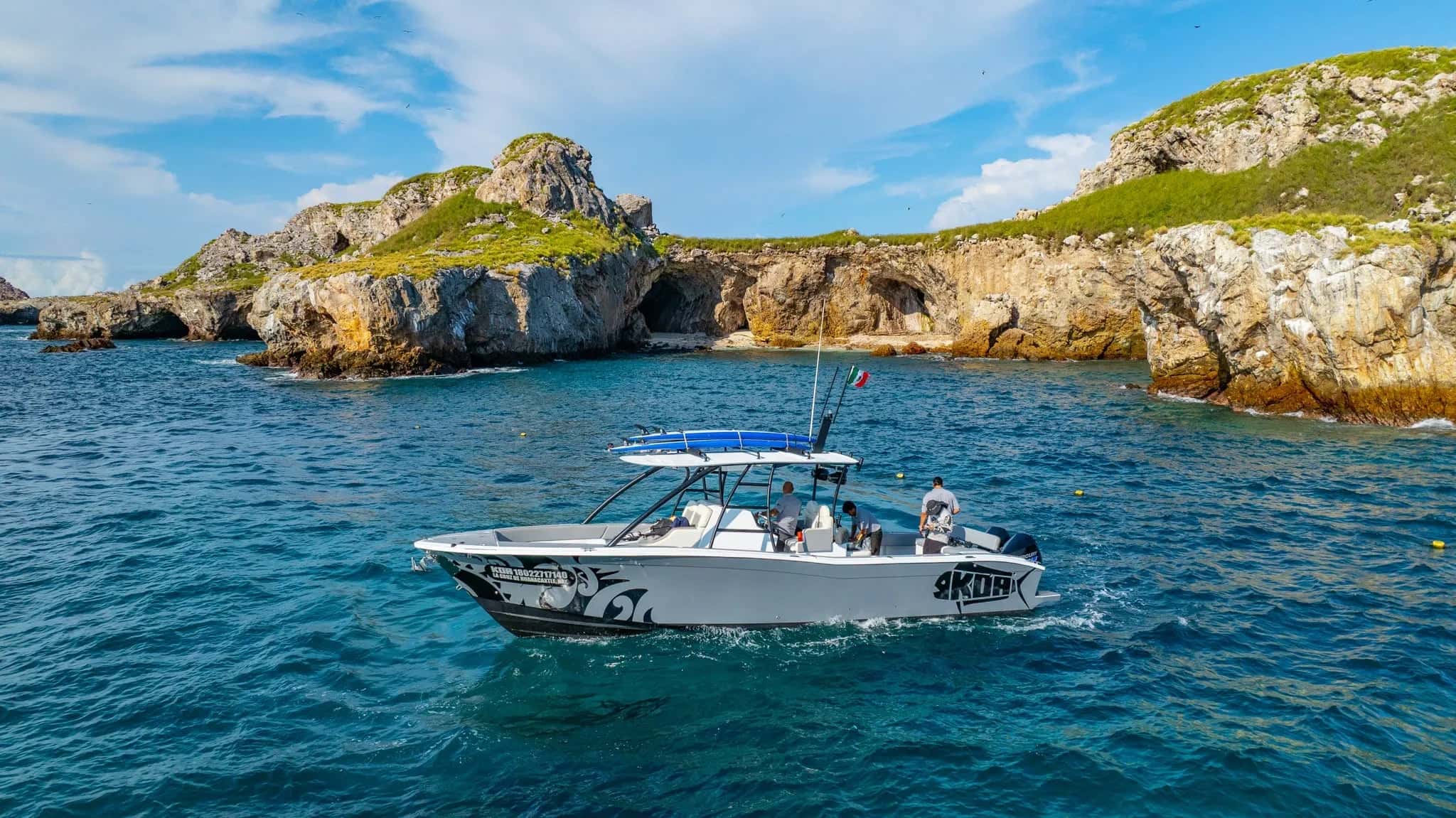 Grey sport boat with a T-top idling below green-topped sea cliffs on turquoise water