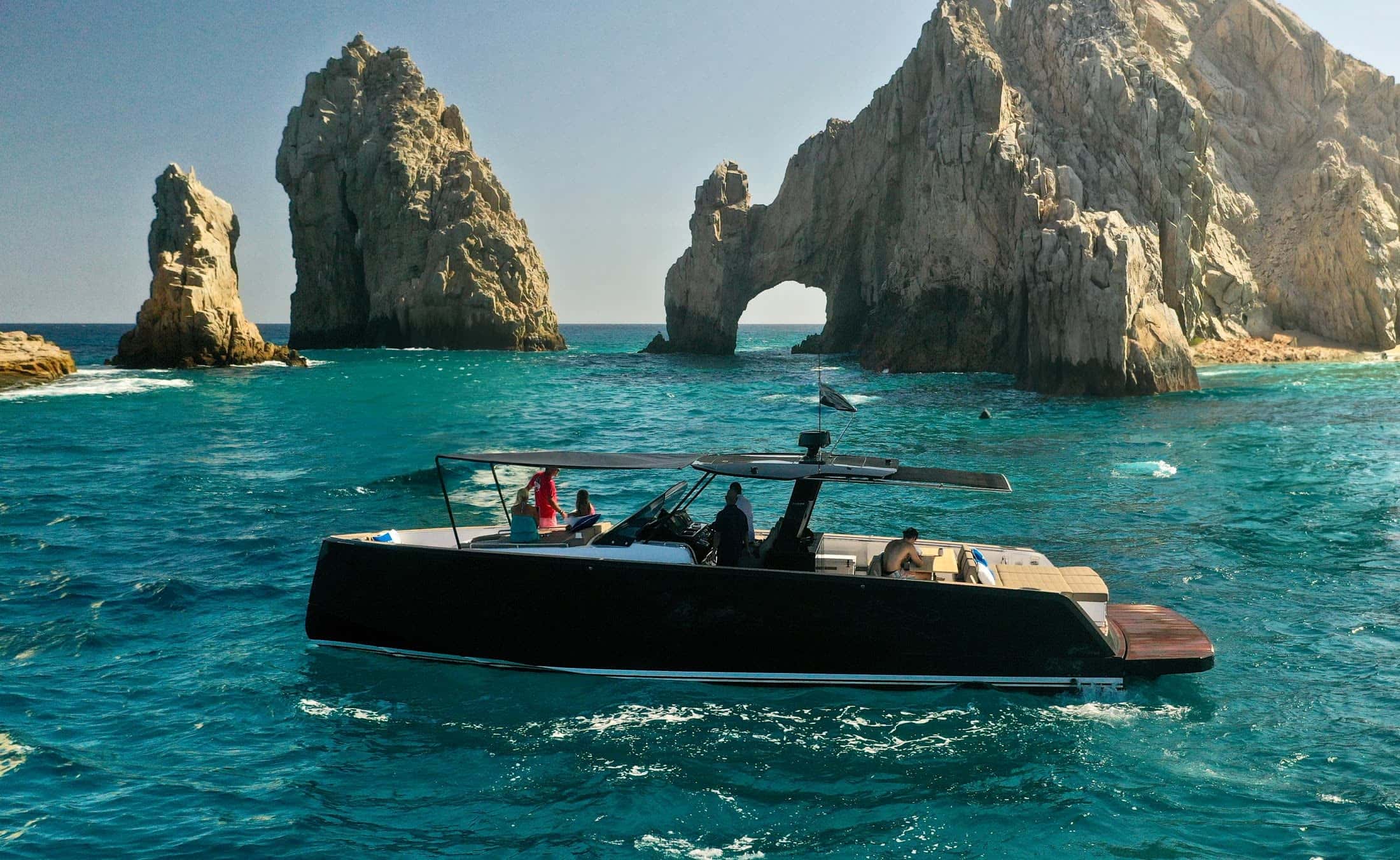 One&Only, a dark Pardo motor yacht with a T-top, cruising beside a rock arch in clear turquoise water