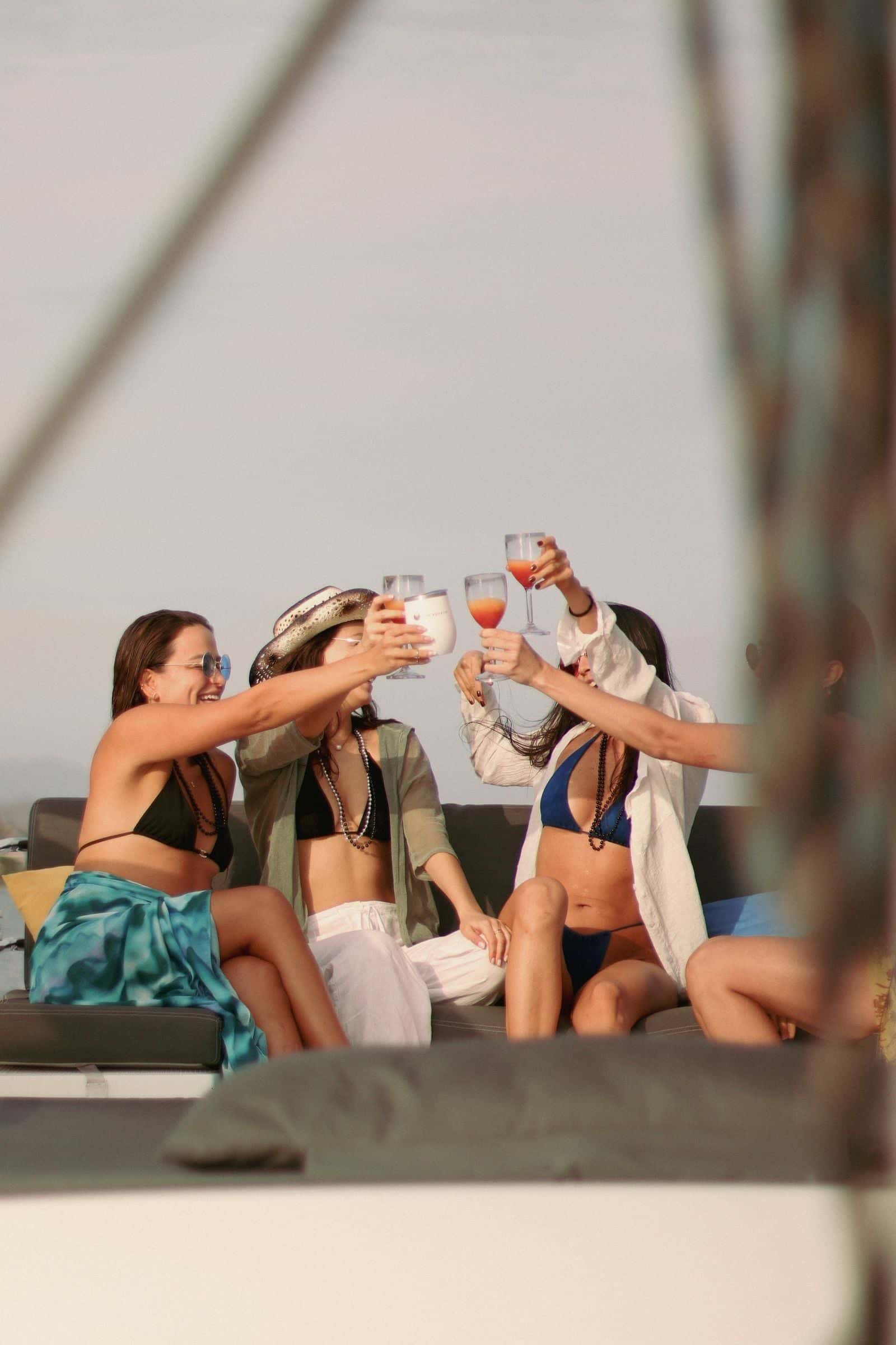 Four friends raising glasses on deck cushions under the sail