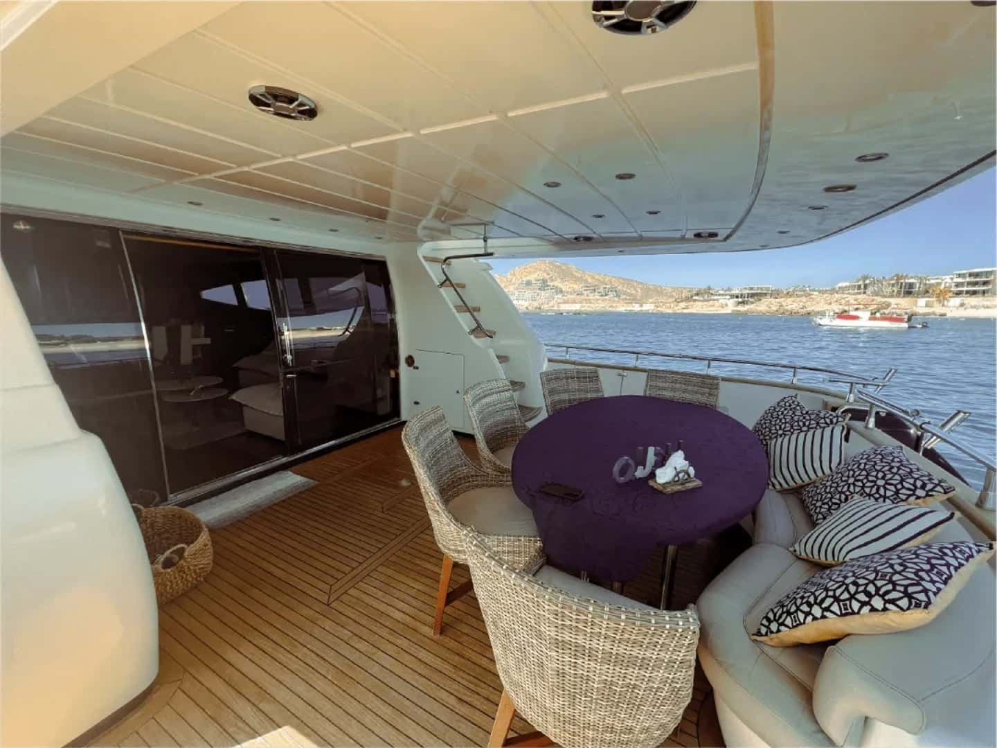 Covered aft deck with a round purple-clothed table, wicker chairs and a cushioned bench