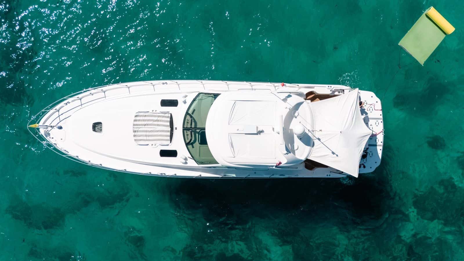 Aerial view of the yacht at anchor over turquoise water, a floating lily pad off her stern