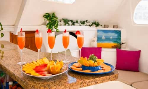 Tropical cocktails and plates of fruit set out on the galley counter, the cushioned saloon bench behind