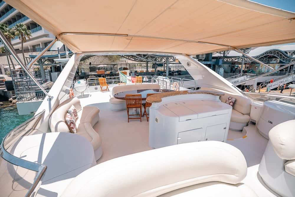 Flybridge under the hardtop with curved white seating, a helm console and a table, the marina behind