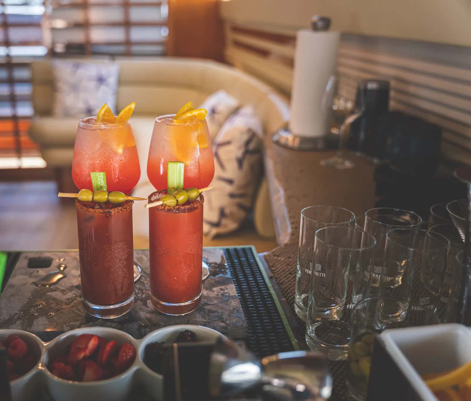 Two garnished Bloody Marys at the saloon bar beside glasses and fruit
