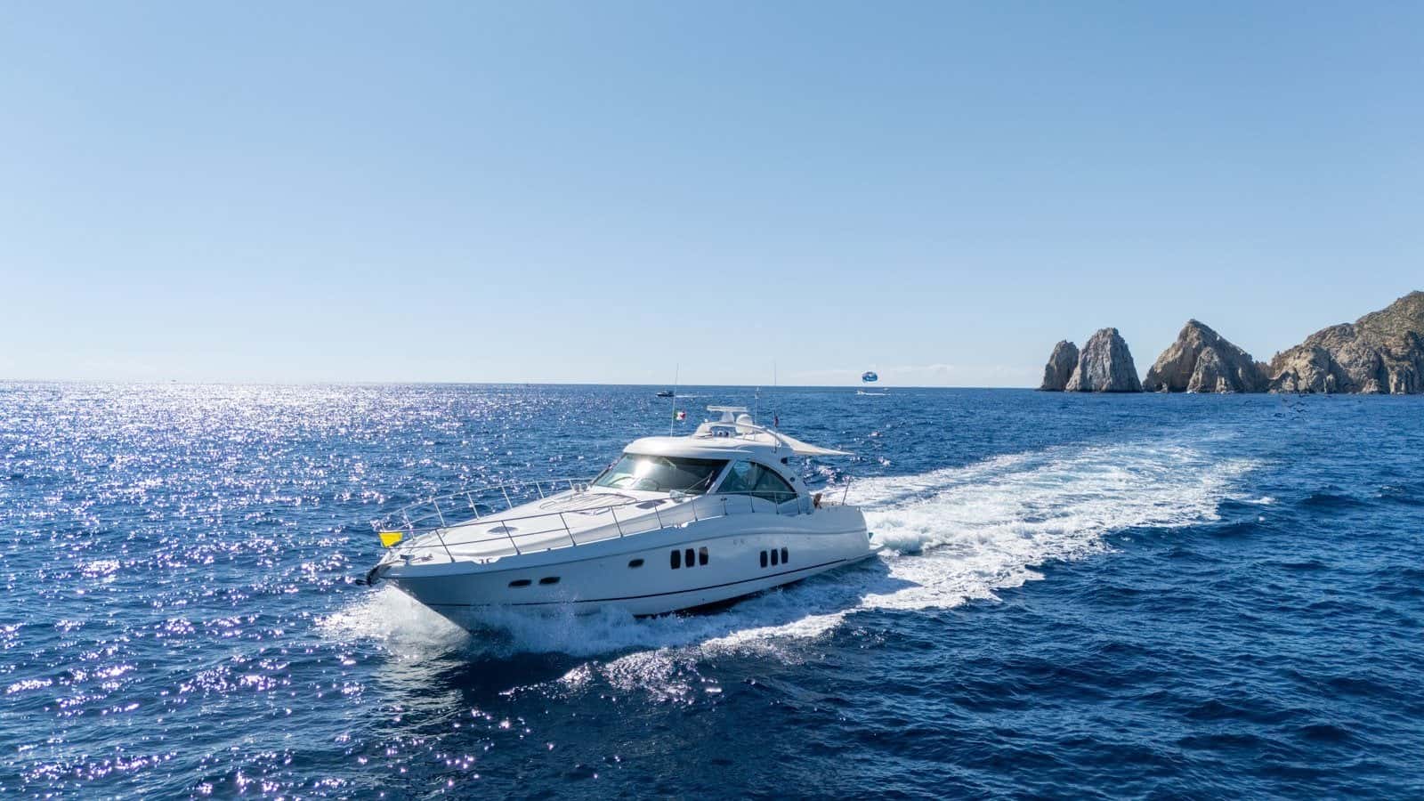 Steel Aweigh under way on blue water, a long white wake behind her and the Arch of Cabo San Lucas on the horizon
