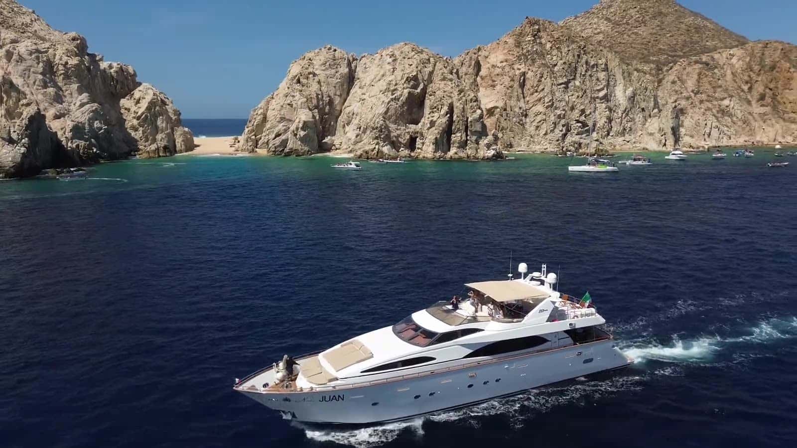 Aerial view of Number Juan cruising on deep blue water below the rocks of the Arch at Land's End