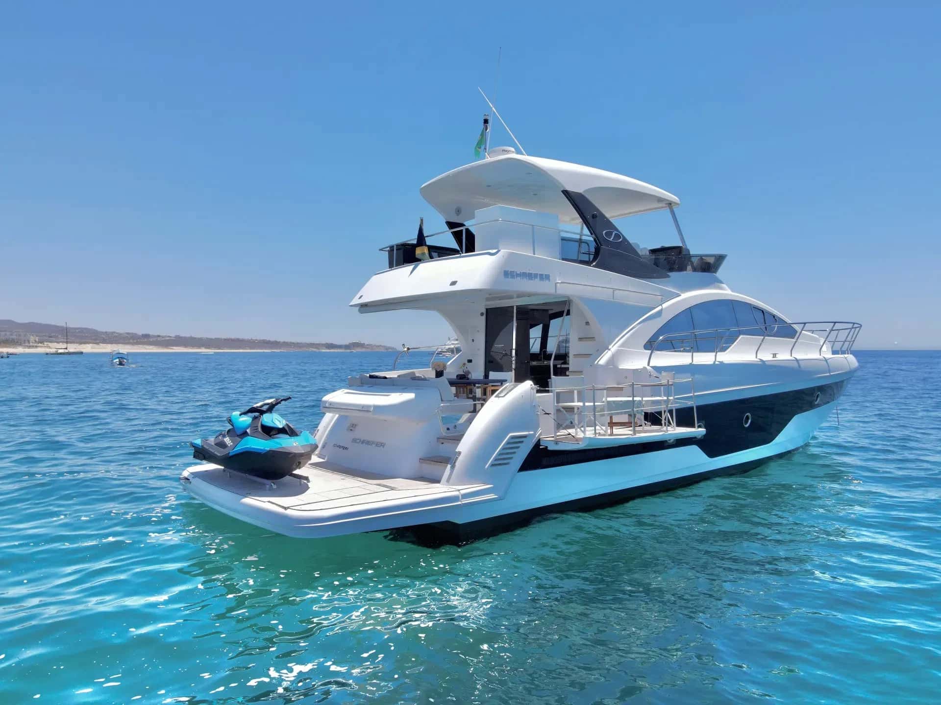 Bleed Blue at anchor in turquoise water, seen from the stern quarter with a jet ski on the swim platform
