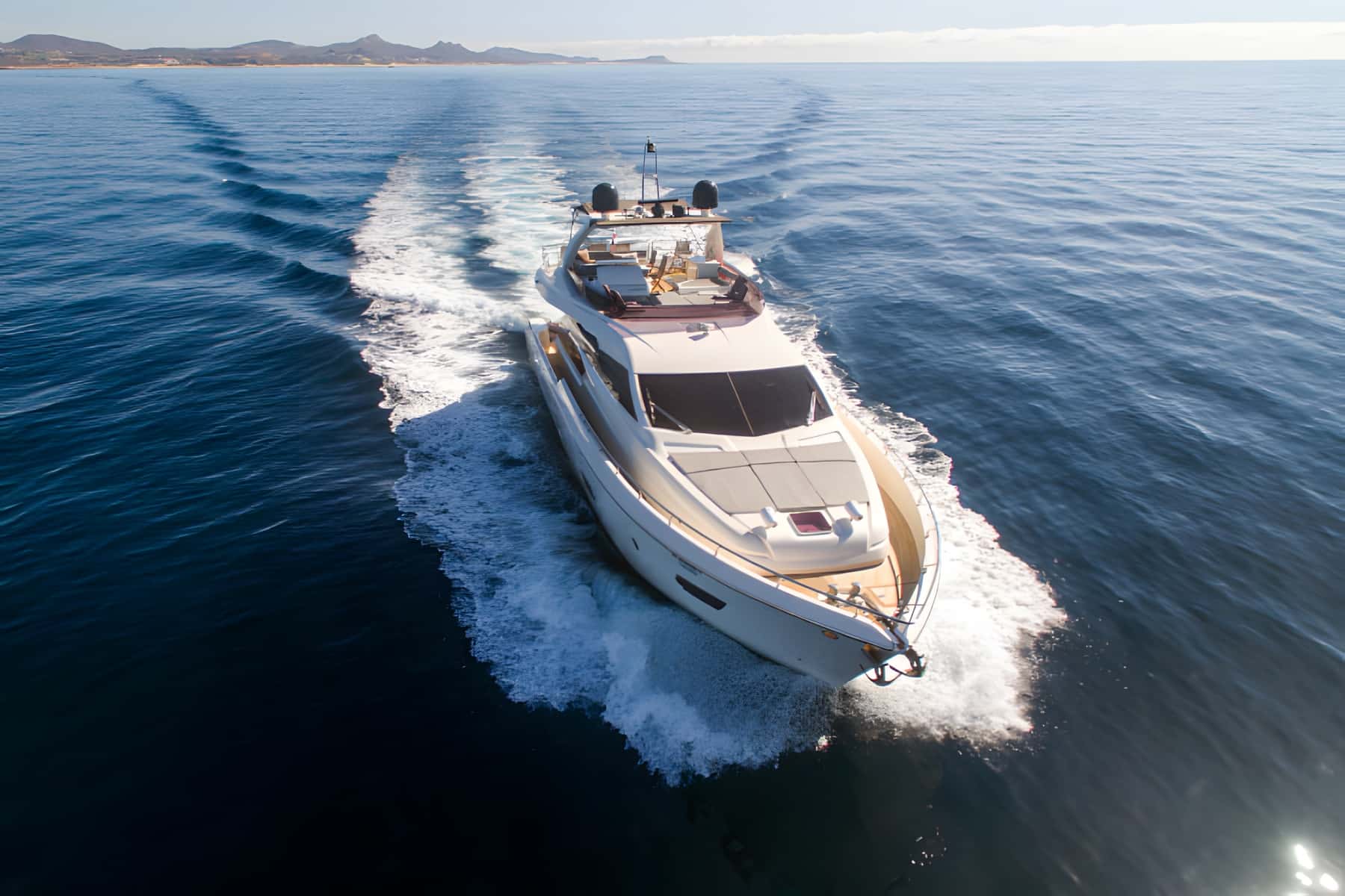 Yacht seen from above, cruising with a white wake and hills behind