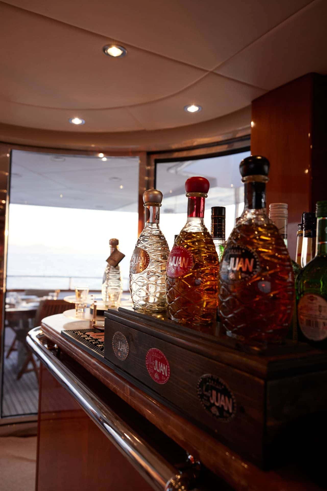 Bottles of the yacht's namesake tequila on the saloon bar, the aft deck through the glass doors