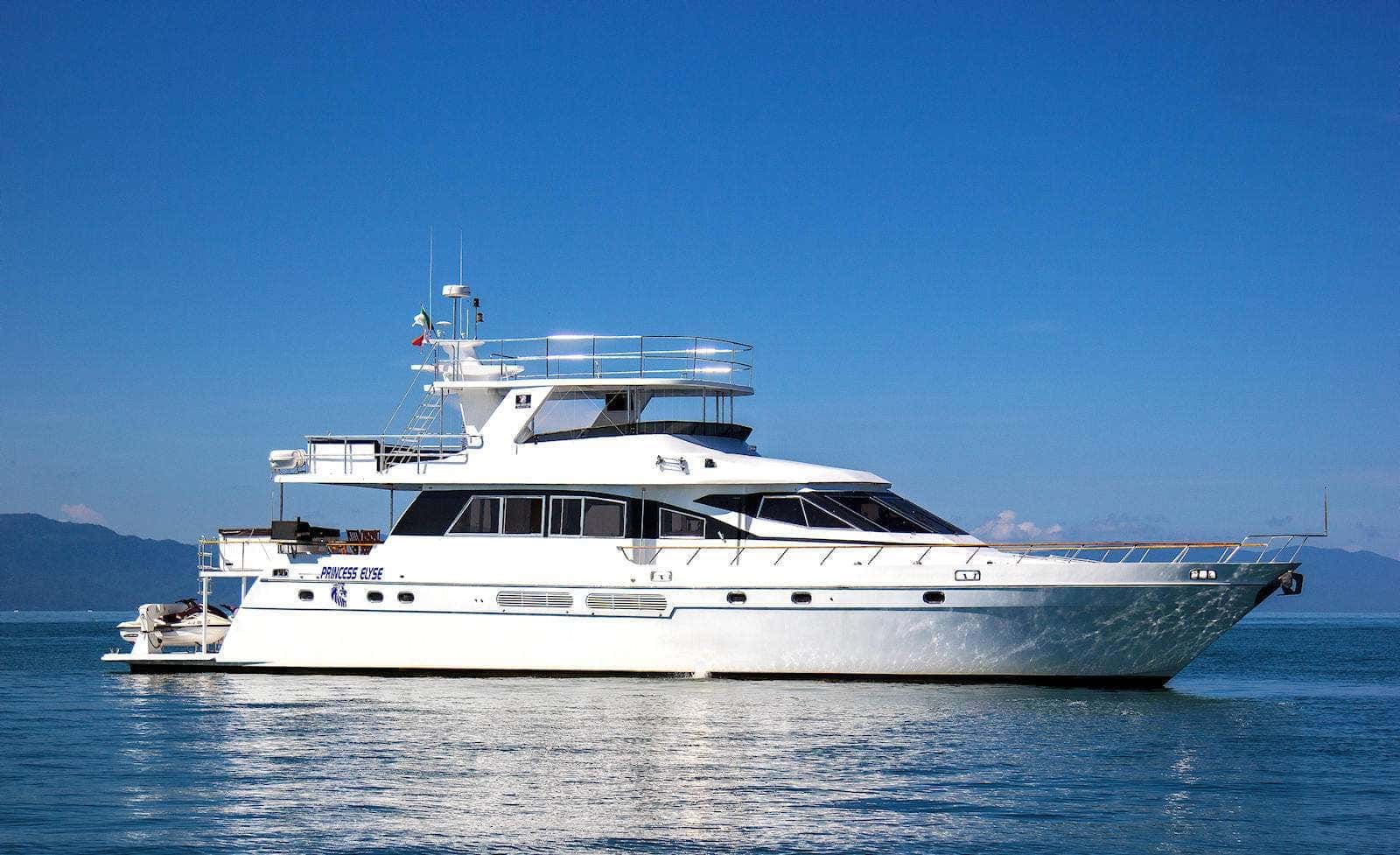 Side profile of the white motor yacht on calm blue water, mountains behind