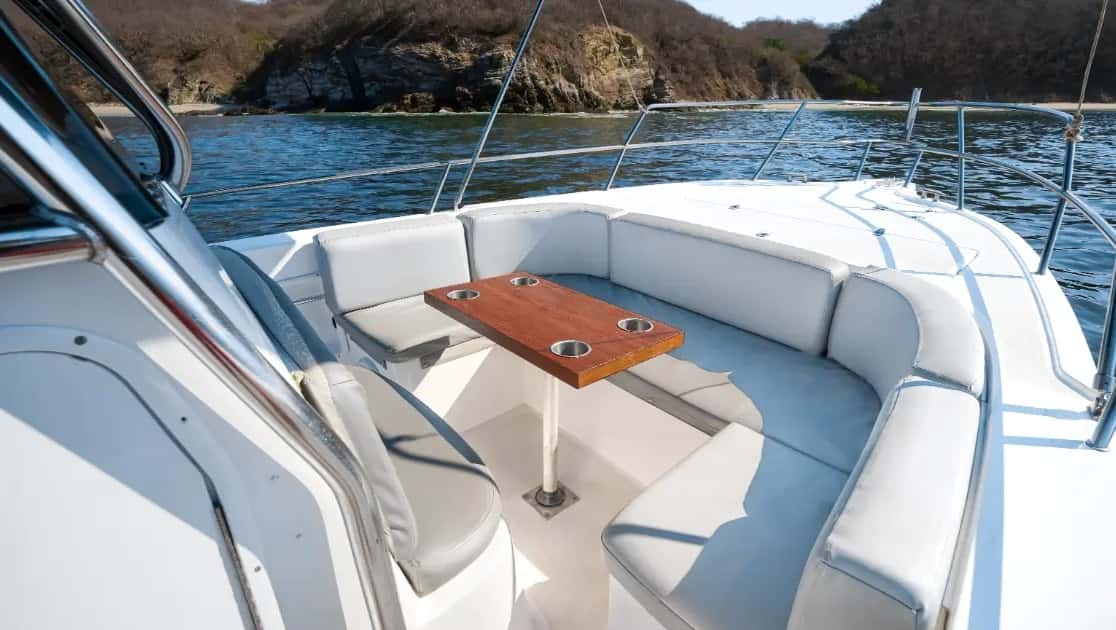 Curved bow seating around a teak table with cup holders, shoreline in the background