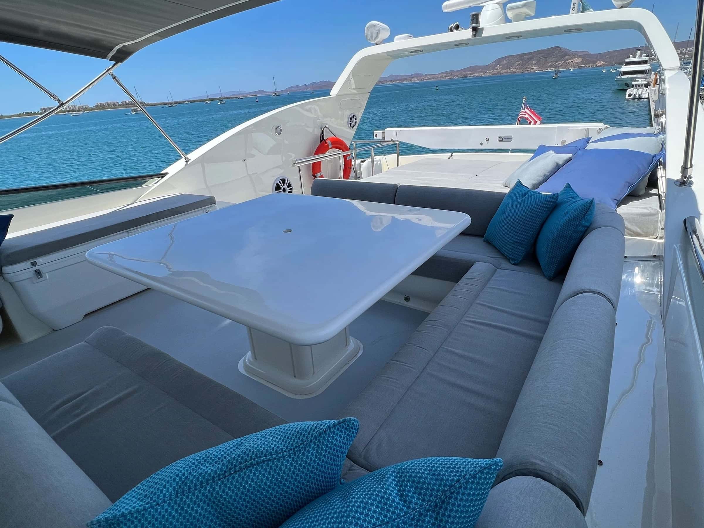 Flybridge dinette with a white table, grey seating and blue cushions under the bimini