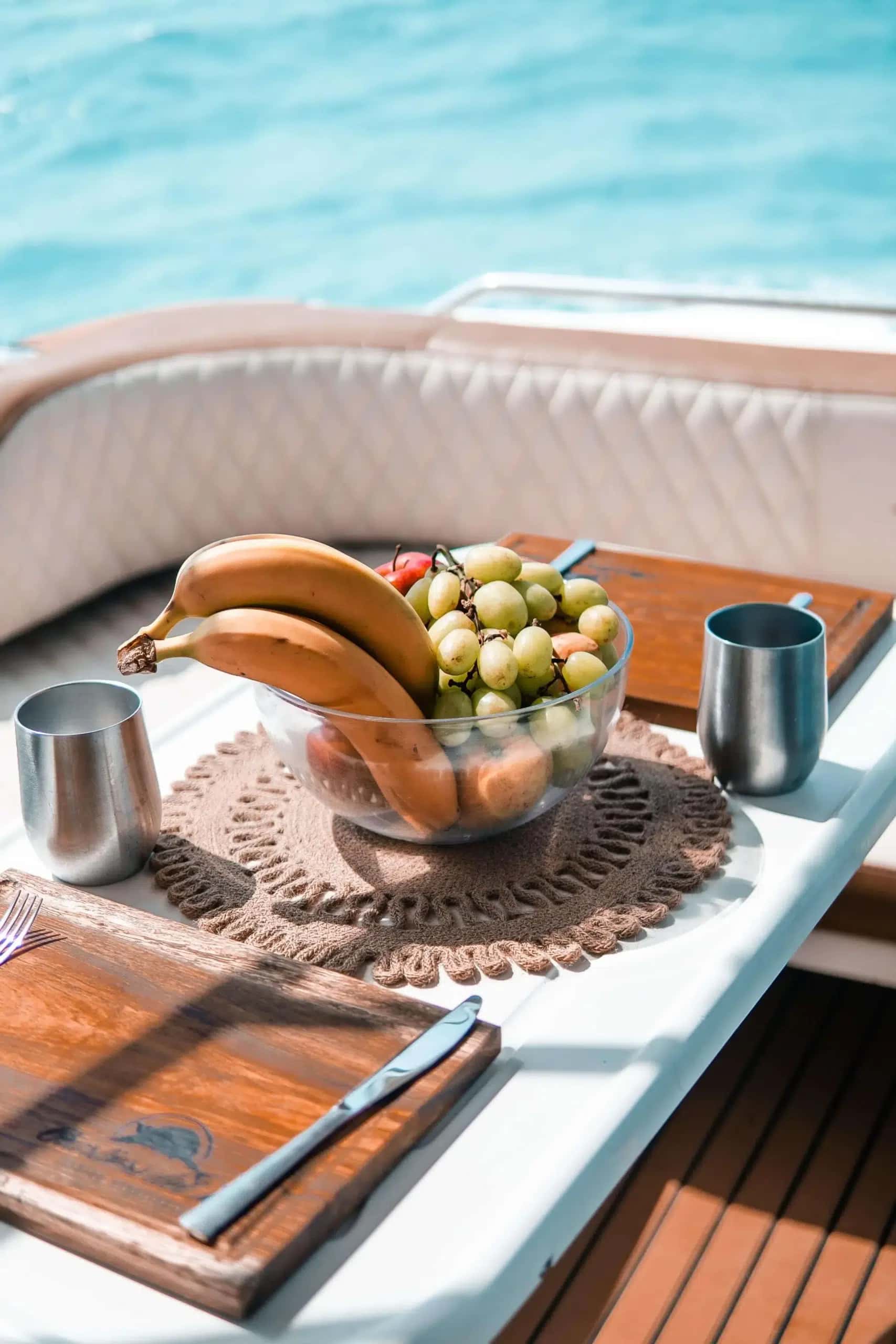 Fruit bowl of bananas and grapes with steel tumblers and serving boards on the cockpit table
