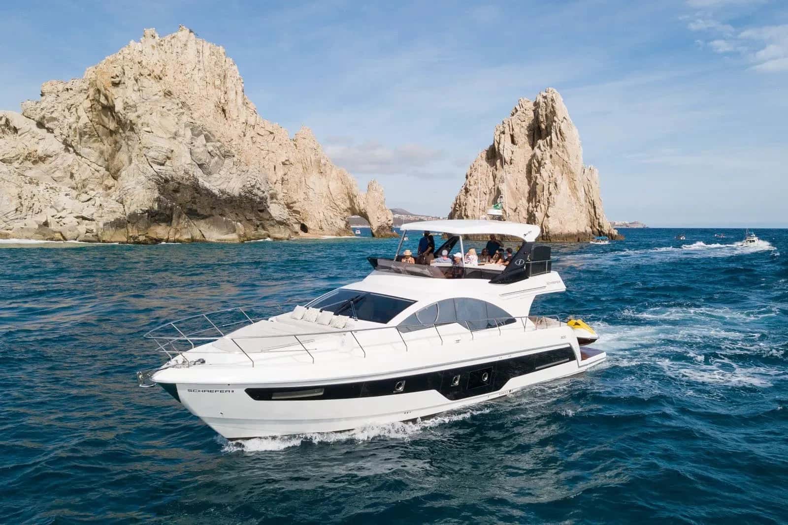 The yacht under way below the rock arch and pinnacles at the tip of the cape
