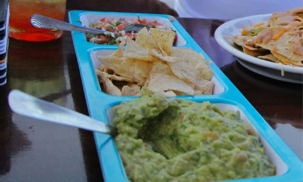 Guacamole, pico de gallo and tortilla chips served in a tray on board